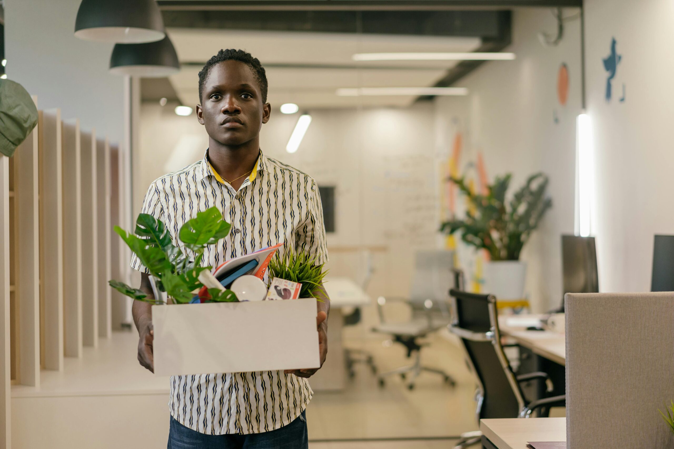 A man carrying a white box filled with his belongings through an office following the Great Resignation 2.0 in 2025, a common sight in January 2025 as workers seek out better work-life balance, employee wellbeing, and talent recognition strategies.